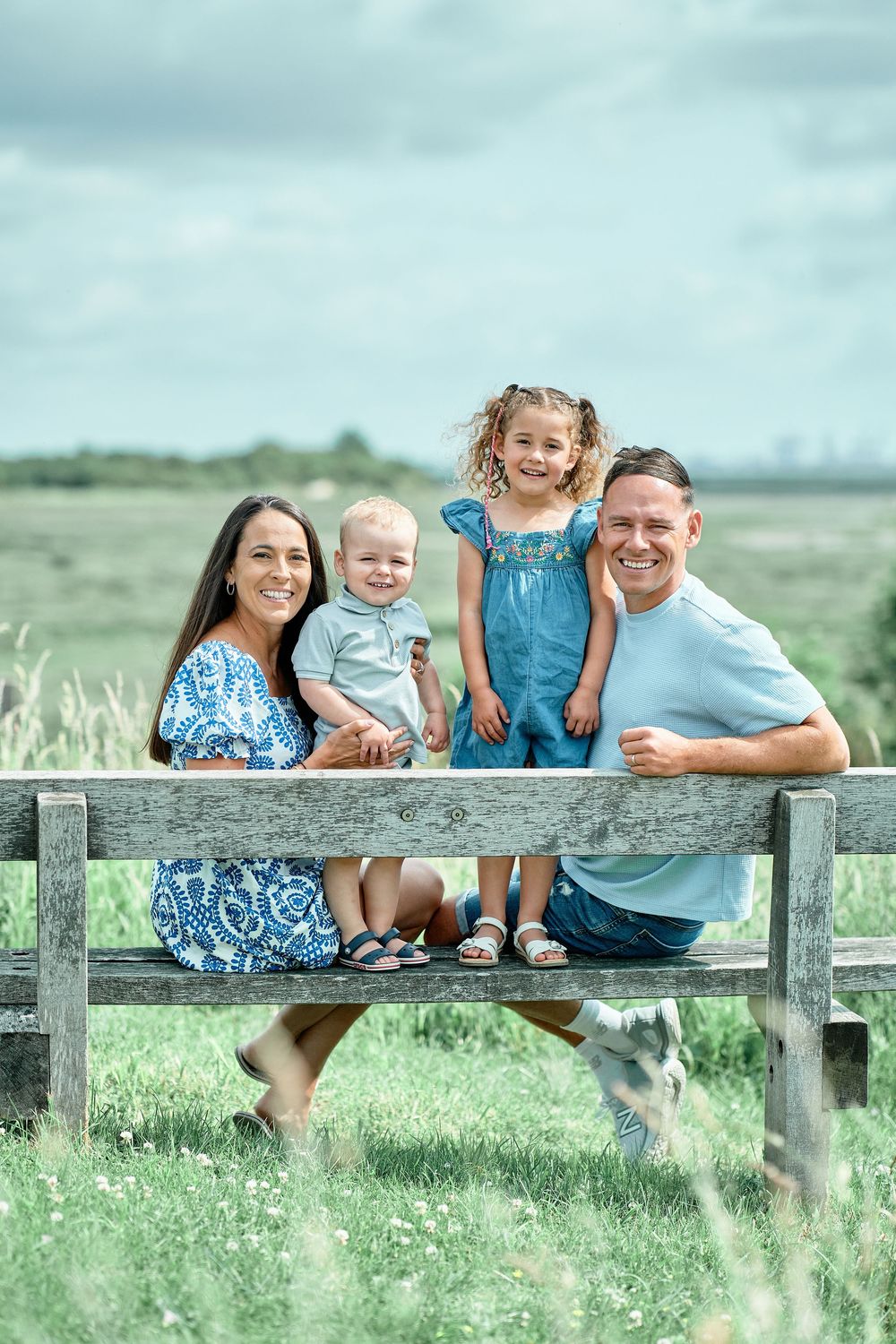 A group sits casually on a wooden fence in a green field wearing coordinated blue and white outfits for a summer photo.