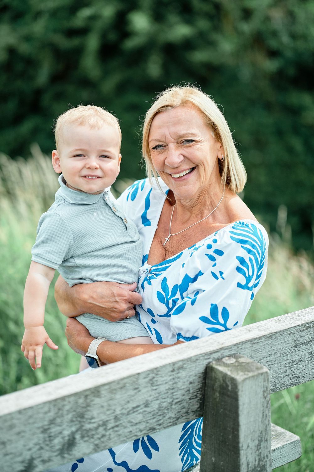 A heartwarming outdoor portrait of two people in coordinating blue and white outfits smiling together on a wooden bench.