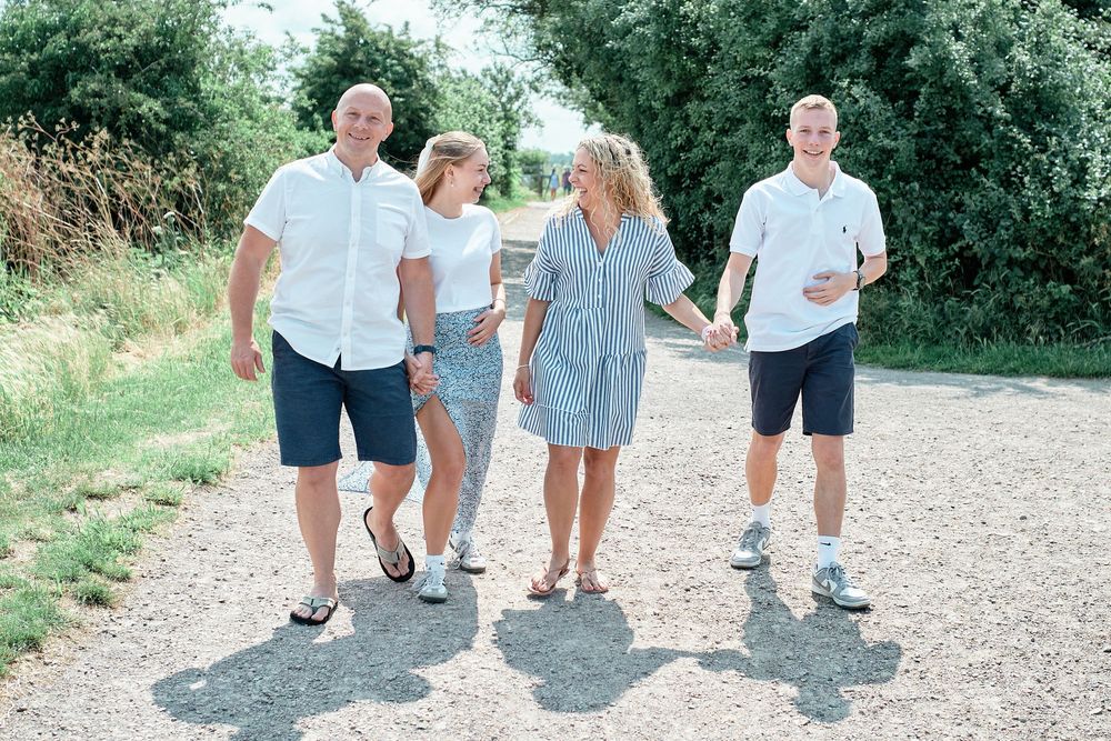 A family of four walks together on a sunny gravel path surrounded by green foliage on a summer day.
