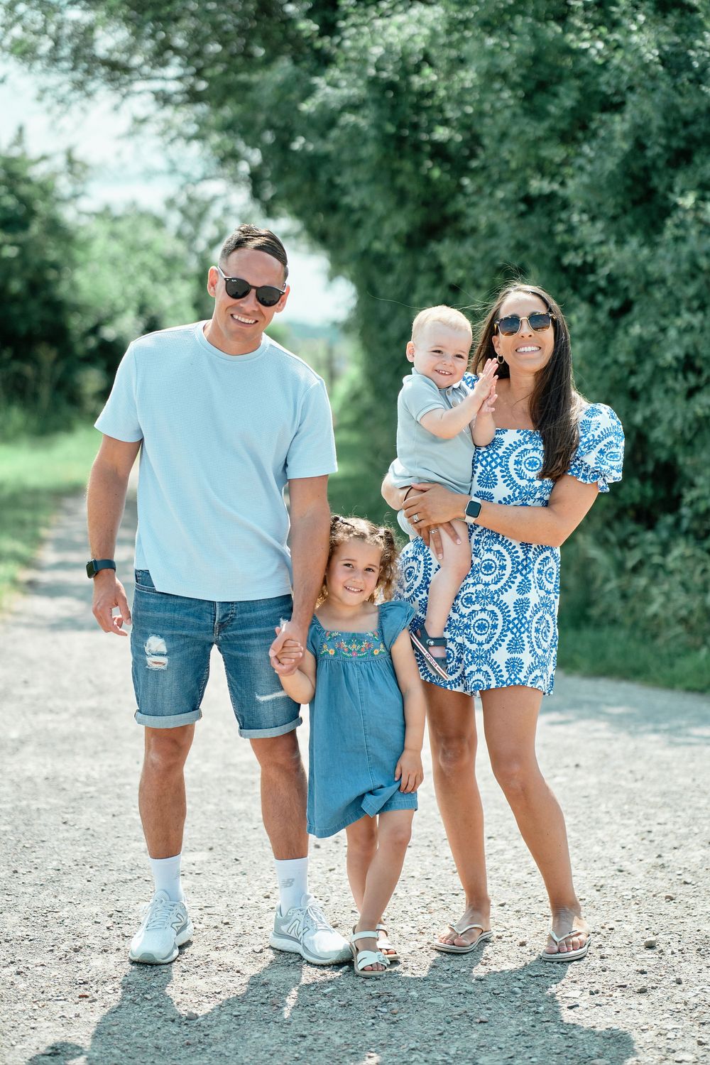 A family wearing coordinated blue and denim outfits poses together on a gravel path in a natural outdoor setting.