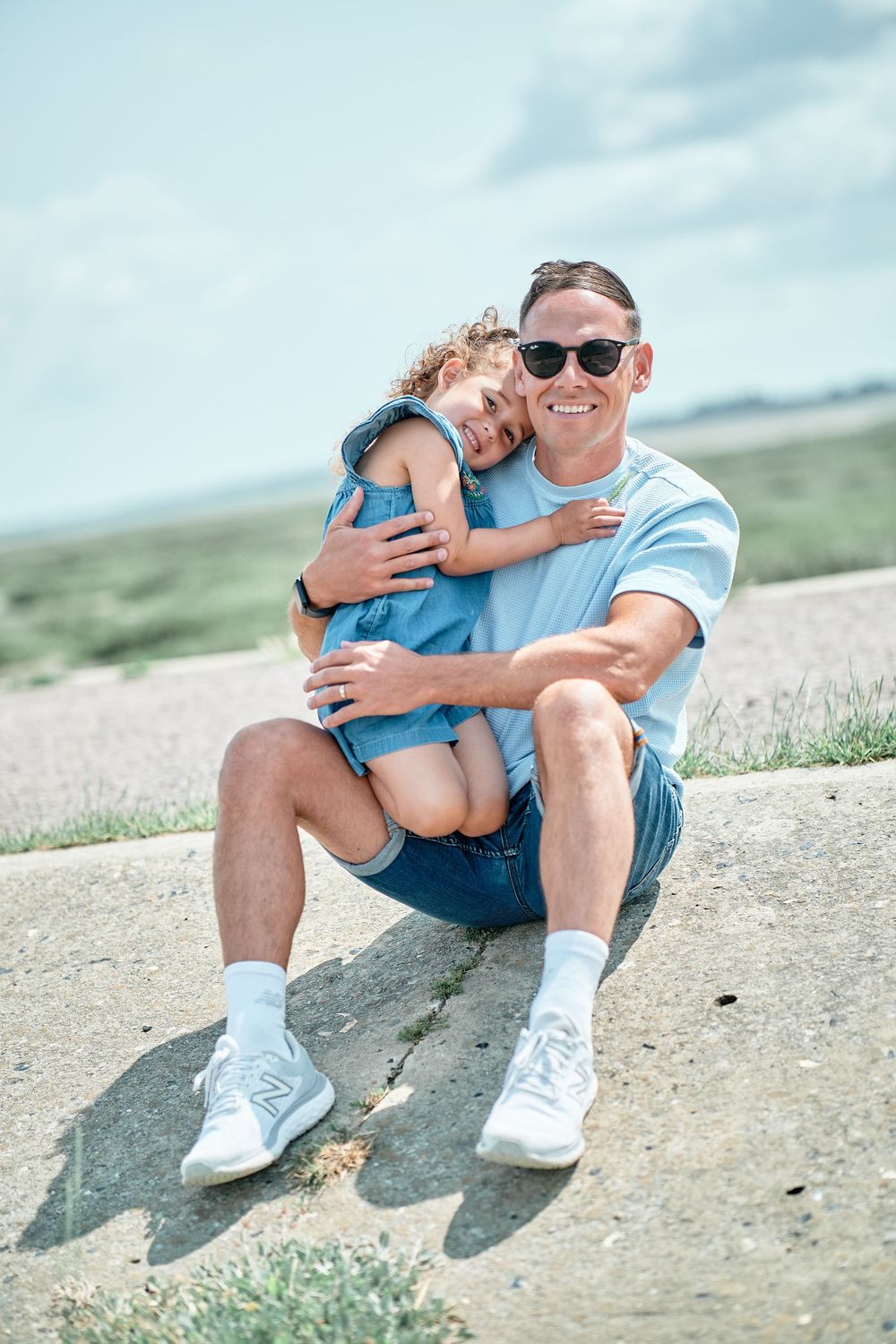 Parent and child sit together on a sandy slope sharing a warm embrace at the beach on a sunny day.