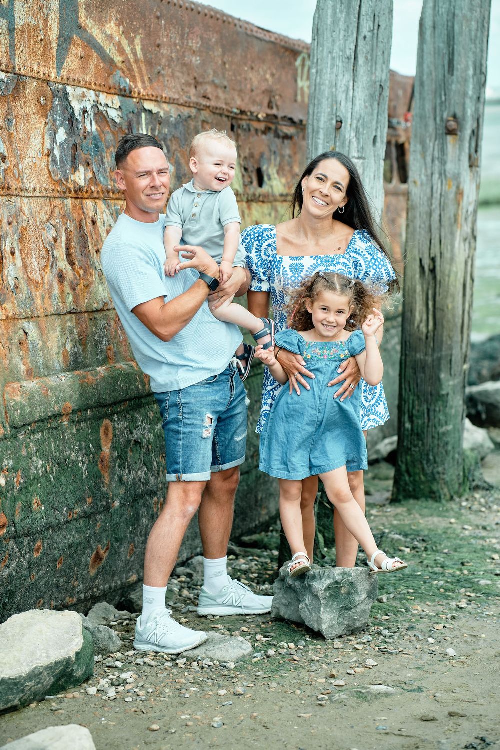 A group poses together outdoors against a rustic wall with weathered green posts on a sunny day.