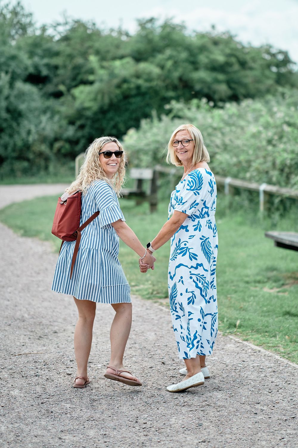 Two people walk hand in hand down a gravel path wearing coordinating blue and white summer outfits.