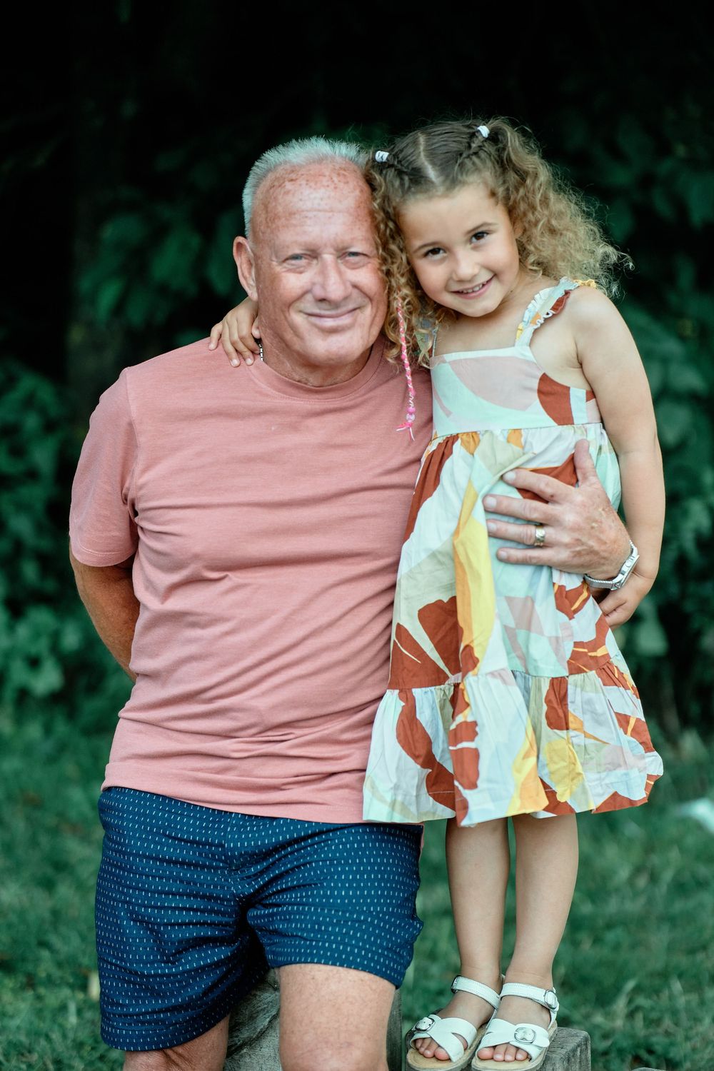 Heartwarming outdoor portrait of two family members sitting together in matching pink and blue outfits in a garden setting.