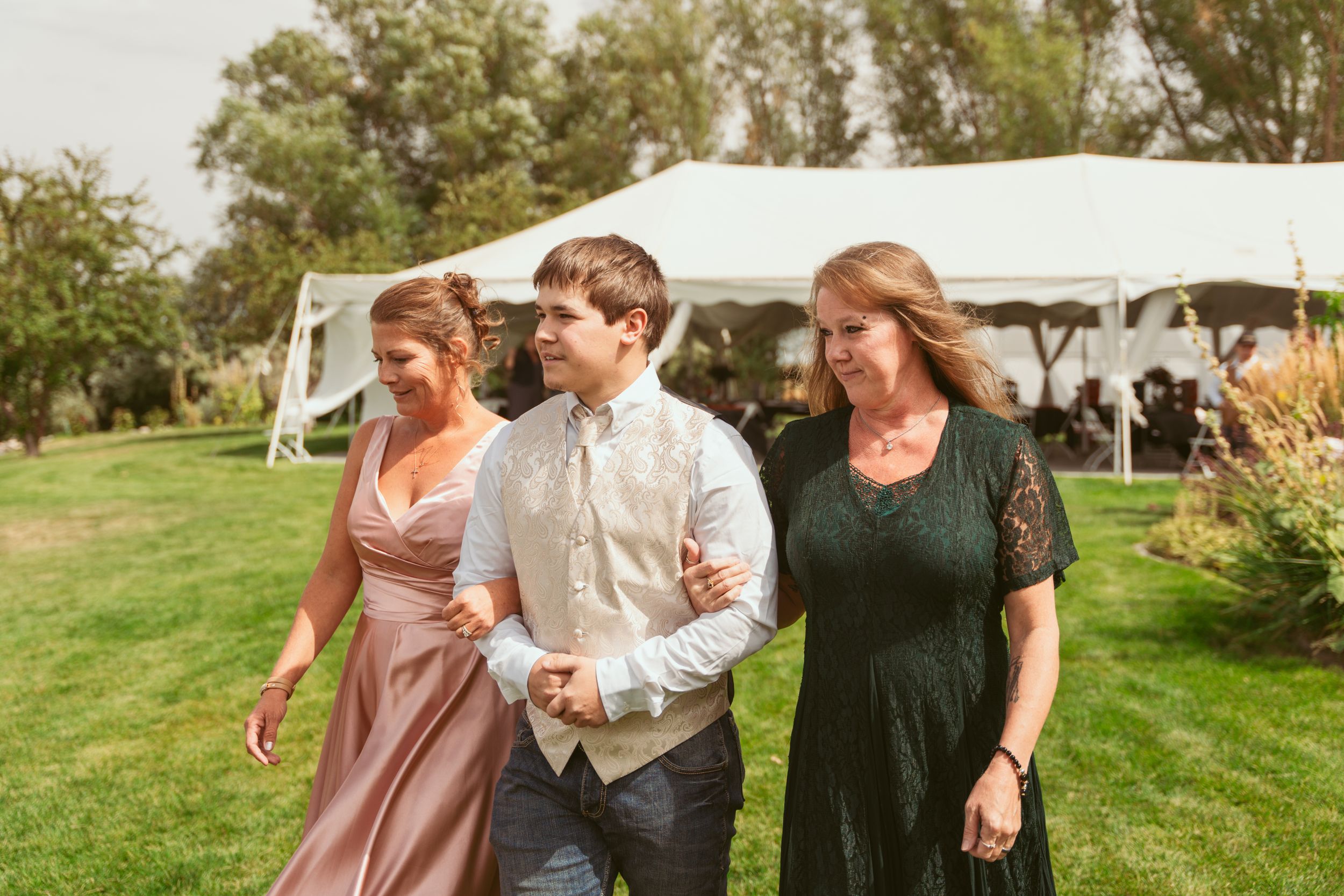 People in casual wedding attire enjoy themselves on a grassy lawn at an outdoor reception.