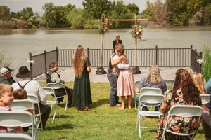 An outdoor wedding ceremony setup by a lake with folding chairs and floral decorations under a cloudy sky.