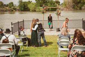 Wedding guests gather for an intimate lakeside ceremony with white chairs and floral decorations.