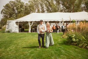 People walk across a lawn towards a white tent reception area decorated for an outdoor wedding celebration.