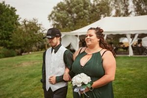 A bridesmaid in a green dress holds a white bouquet next to a groomsman at an outdoor wedding reception.