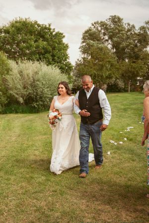 Wedding party members walk on grass near rustic decorations during a casual outdoor celebration.