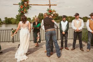 Wedding ceremony taking place on an outdoor deck with a rustic wooden arch and floral decorations.