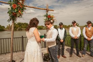 Wedding ceremony in progress at a waterfront venue under a wooden archway adorned with autumn flowers.