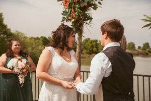 A lakeside outdoor wedding ceremony takes place under a floral arch with sage green bridesmaid dress details.