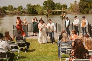 Small outdoor wedding reception by a lake with folding chairs set up on the grass.