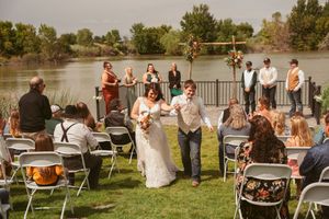 Outdoor wedding ceremony by a lake with white folding chairs and guests watching the proceedings.