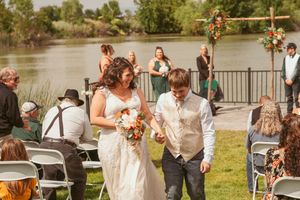 Wedding party exits down the aisle at lakeside venue while guests seated in folding chairs look on.
