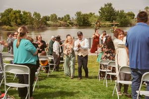 Wedding guests mingle on a lawn during an outdoor reception by a lake.