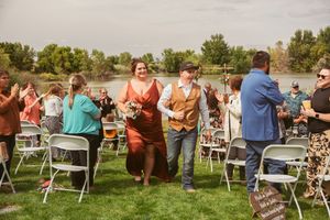 Wedding guests in formal attire stand and applaud during an outdoor reception by the water.