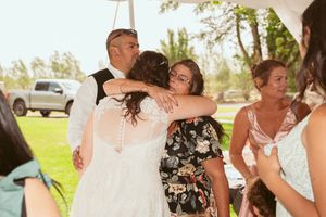 Wedding guests embrace in an emotional moment during an outdoor celebration on a sunny day.