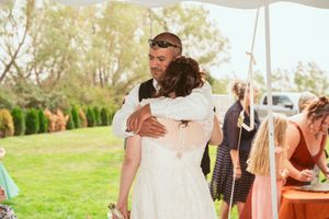 Guests celebrate under a white tent during an outdoor wedding reception.