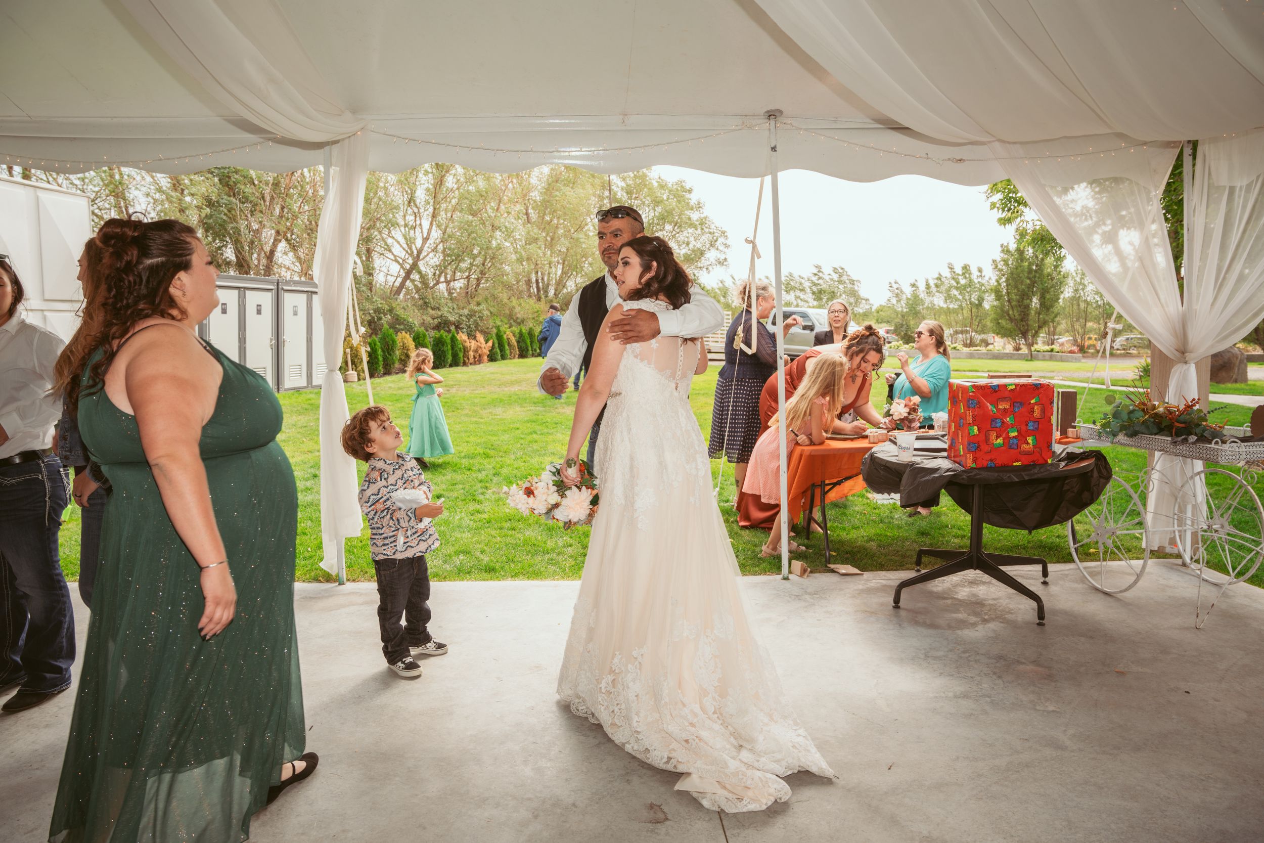 A wedding reception under a white tent with guests dancing on a covered outdoor patio.