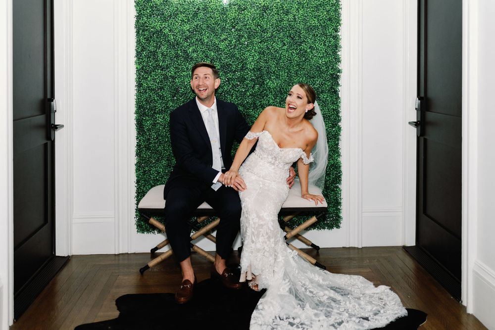 A wedding couple dances and laughs together in a formal white-walled room during their first dance.
