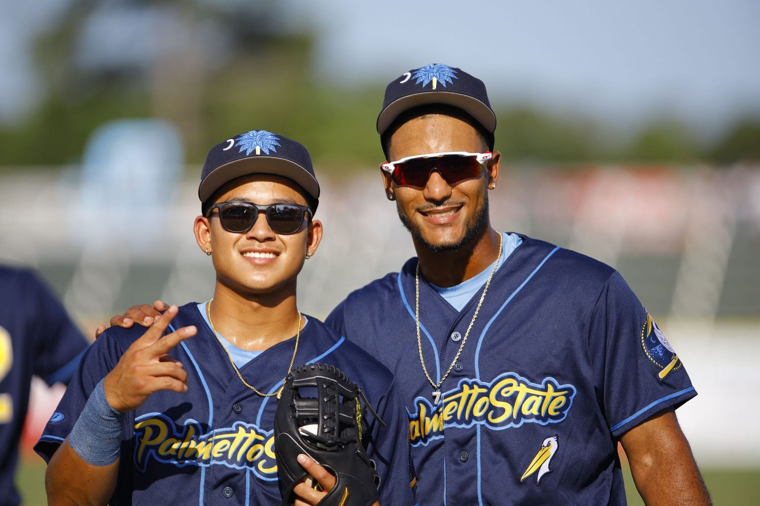 Baseball players in navy blue uniforms and sunglasses pose together on a sunny day at the ballpark.