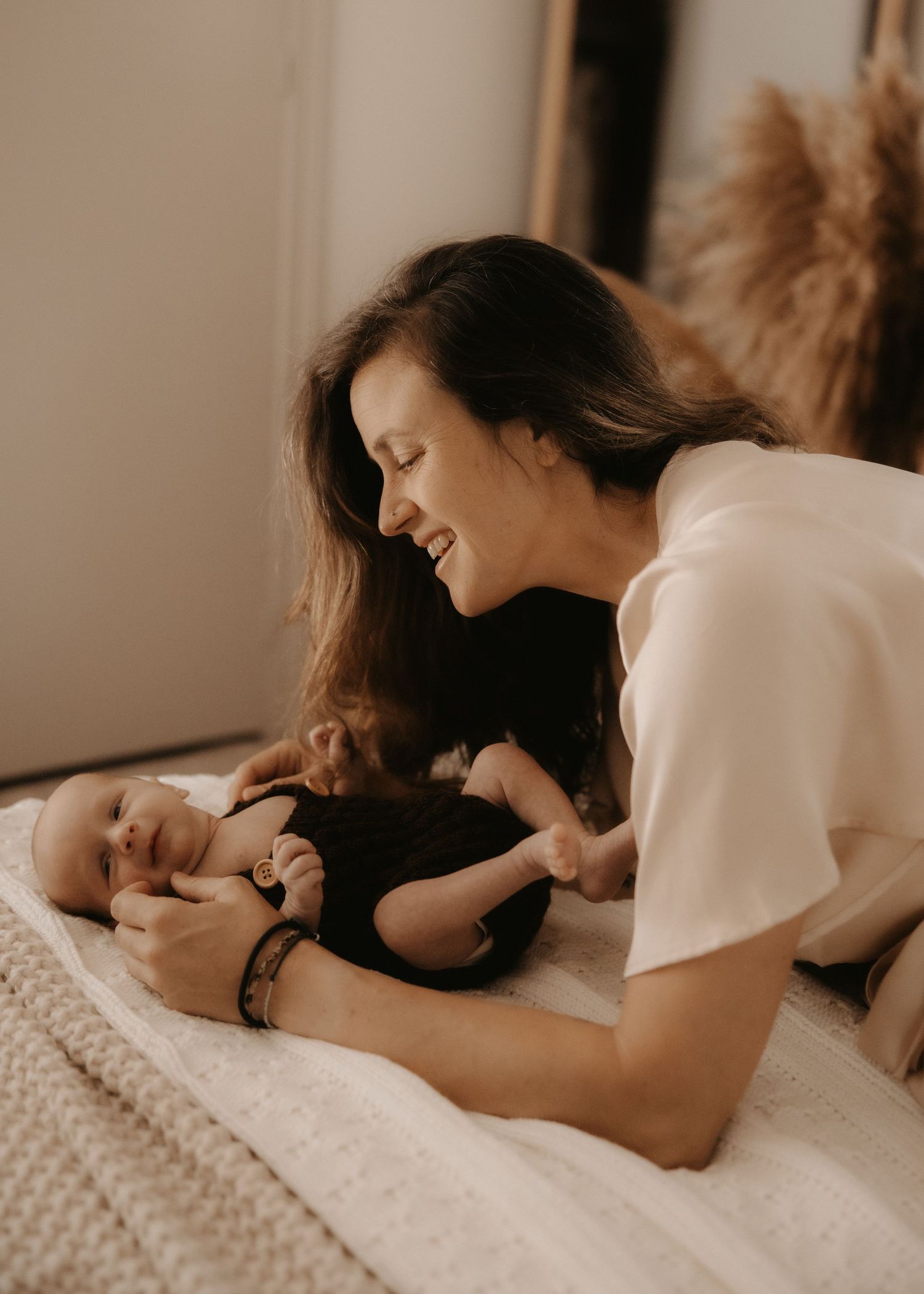 A smiling mother leans over her newborn baby lying on a white blanket, sharing a tender moment.