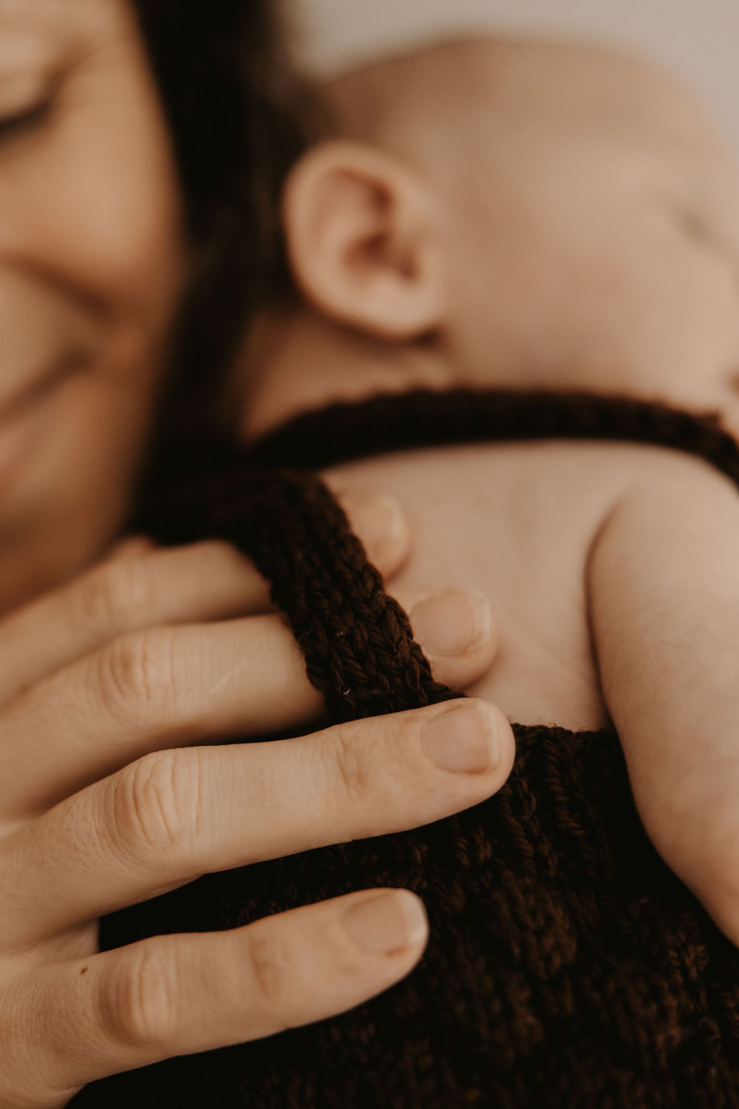 Close-up of a mother tenderly holding her newborn baby wrapped in a dark knit blanket.