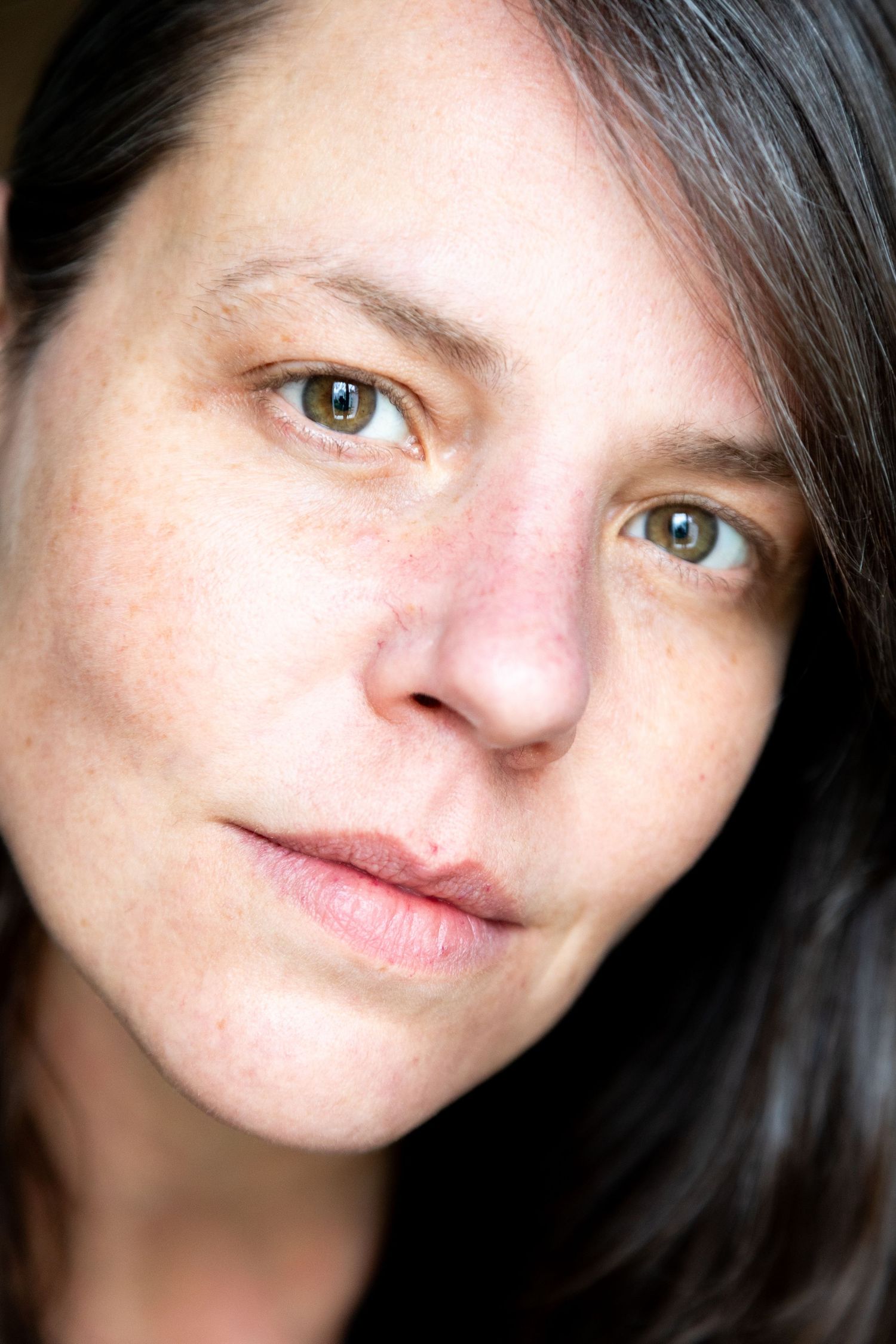 Portrait photo against brown background showing someone with long dark hair wearing a black top in natural lighting.