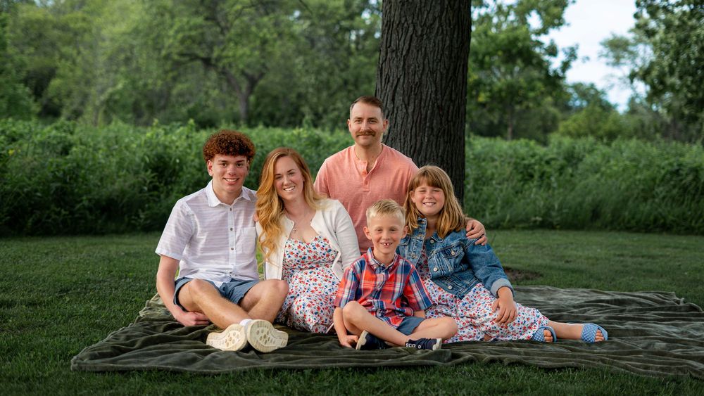 Family sitting together outdoors on the grass during the Conner family portrait session.