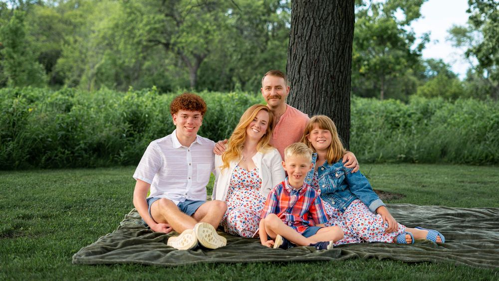 Family sitting together outdoors on the grass during the Conner family portrait session.