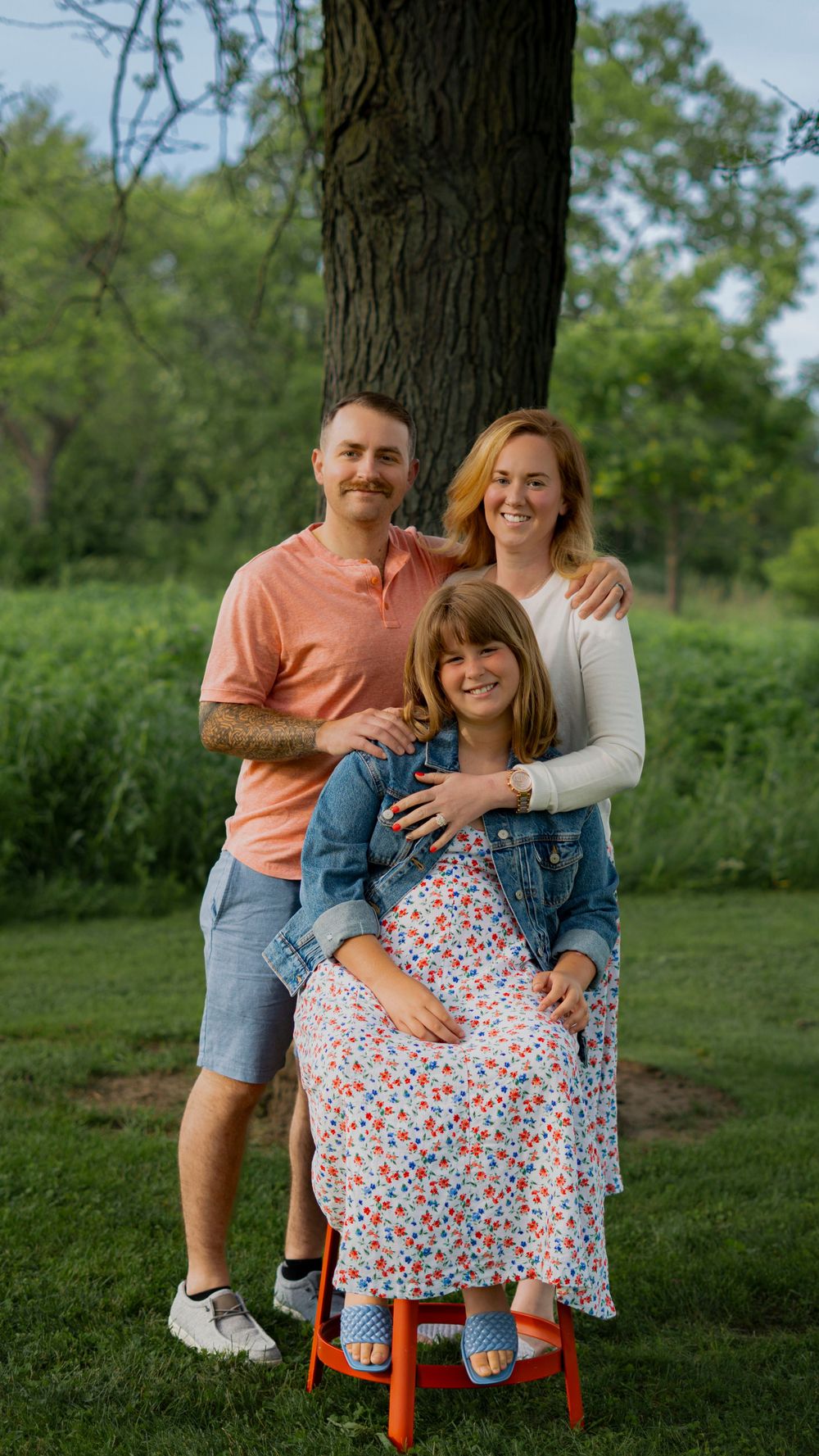 Parents holding their baby outdoors near a tree during a family portrait session.