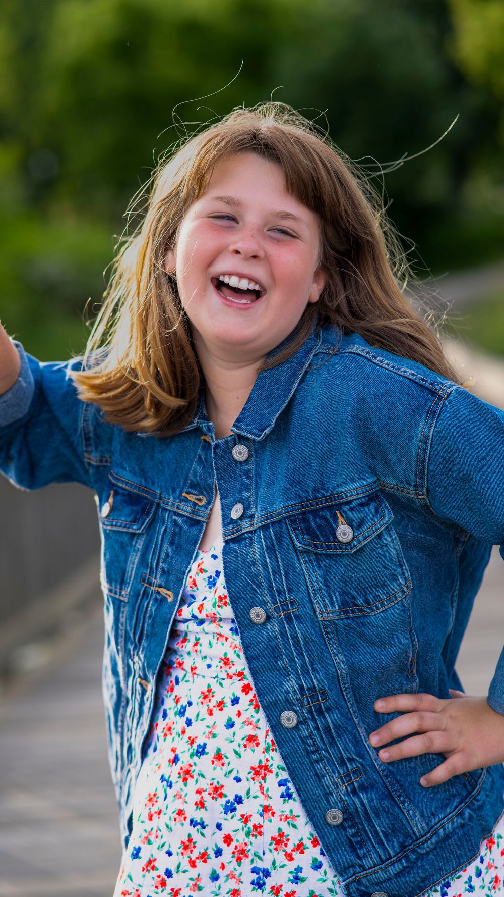 Woman in a blue floral dress laughing outdoors during a portrait session.