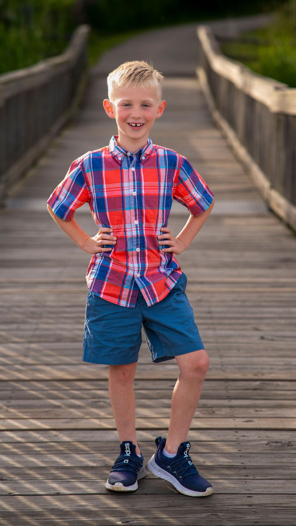 Young boy in a plaid shirt and blue shorts standing outdoors during a family portrait session.