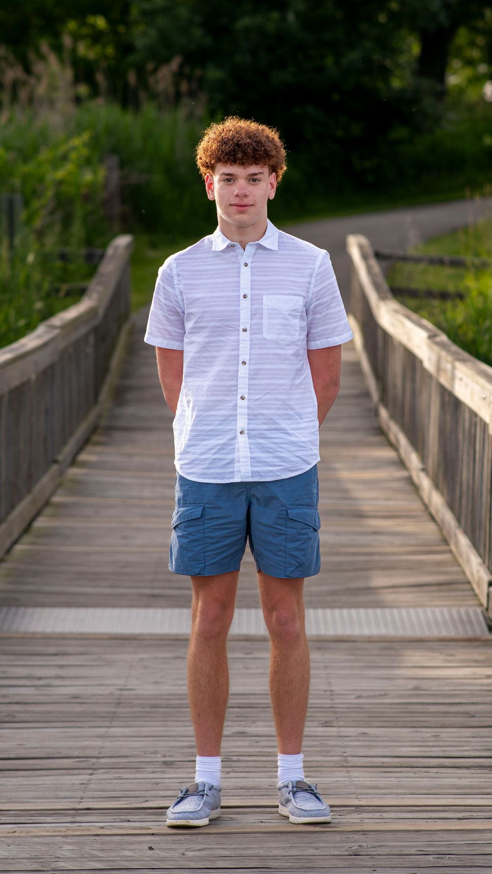 Boy in a white shirt and blue shorts standing on a wooden boardwalk during a family portrait session.