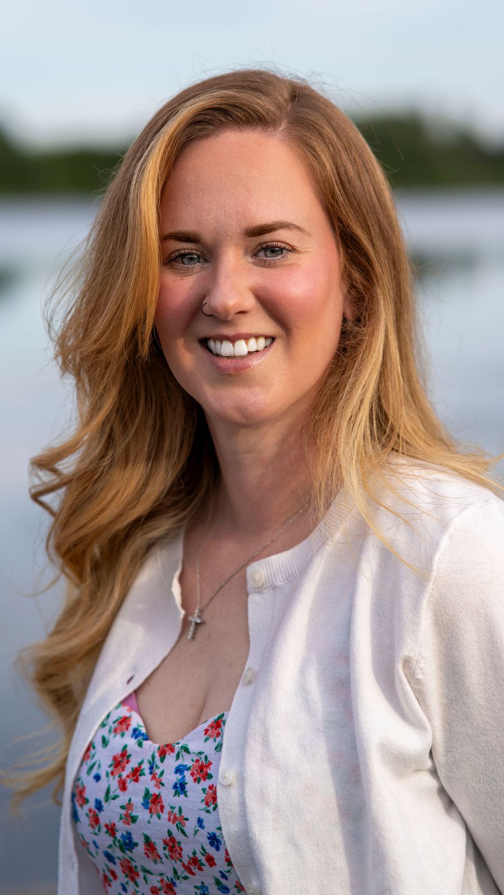 Woman in a white cardigan smiling outdoors during a portrait session.