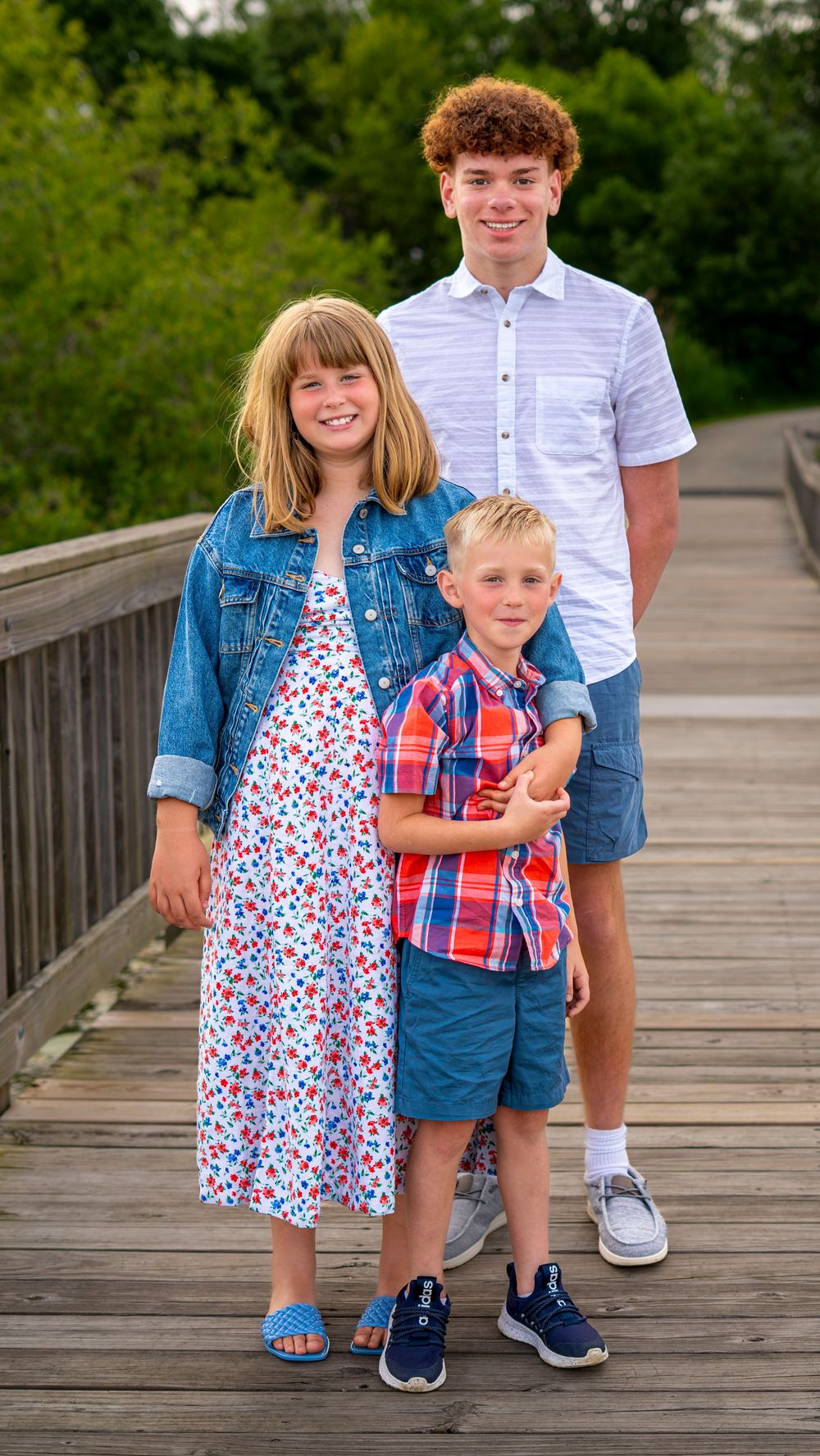Brother standing with two sibling during a family portrait session.