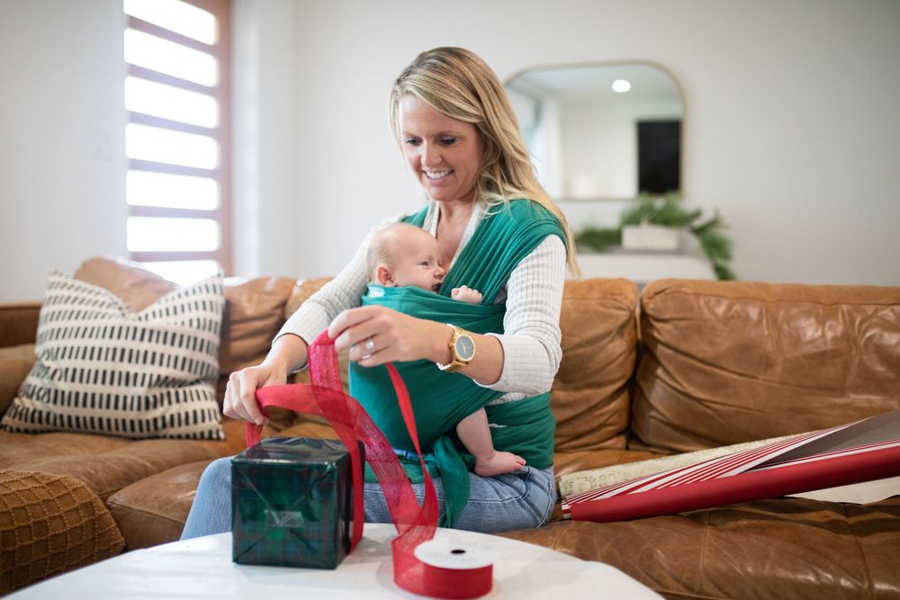 Parent and baby with baby carrier organizing supplies on brown leather couch.
