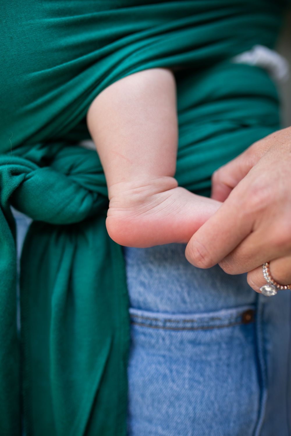 Close up of baby's tiny foot peeking out from emerald green baby wrap against denim.