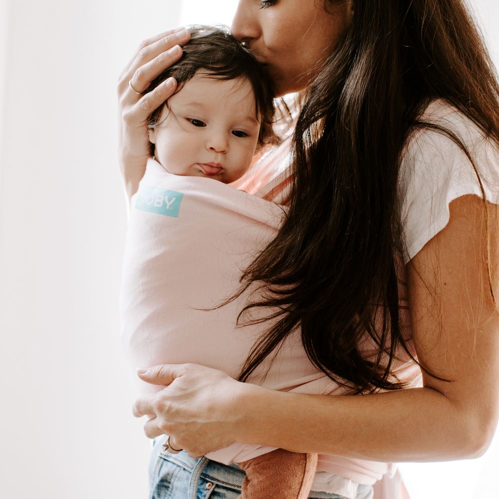 A gentle moment showing babywearing in a soft pink wrap carrier.
