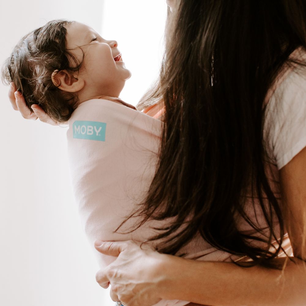 A joyful moment showing laughter while babywearing in a light pink carrier.