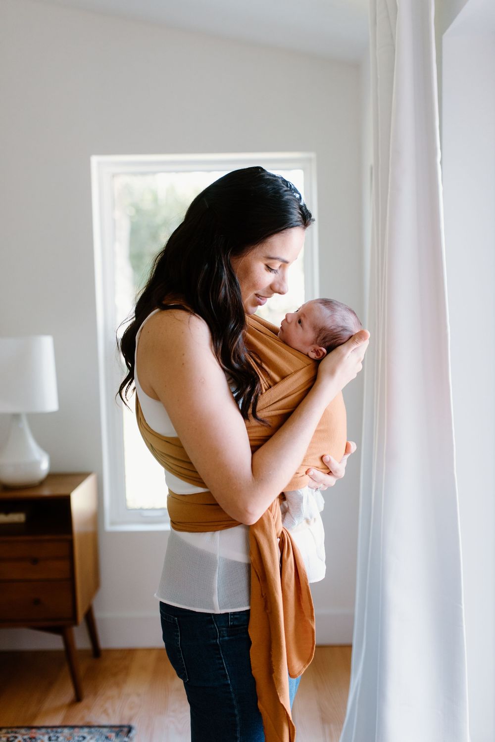 A tender moment between parent and baby in a warm tan-colored baby wrap.