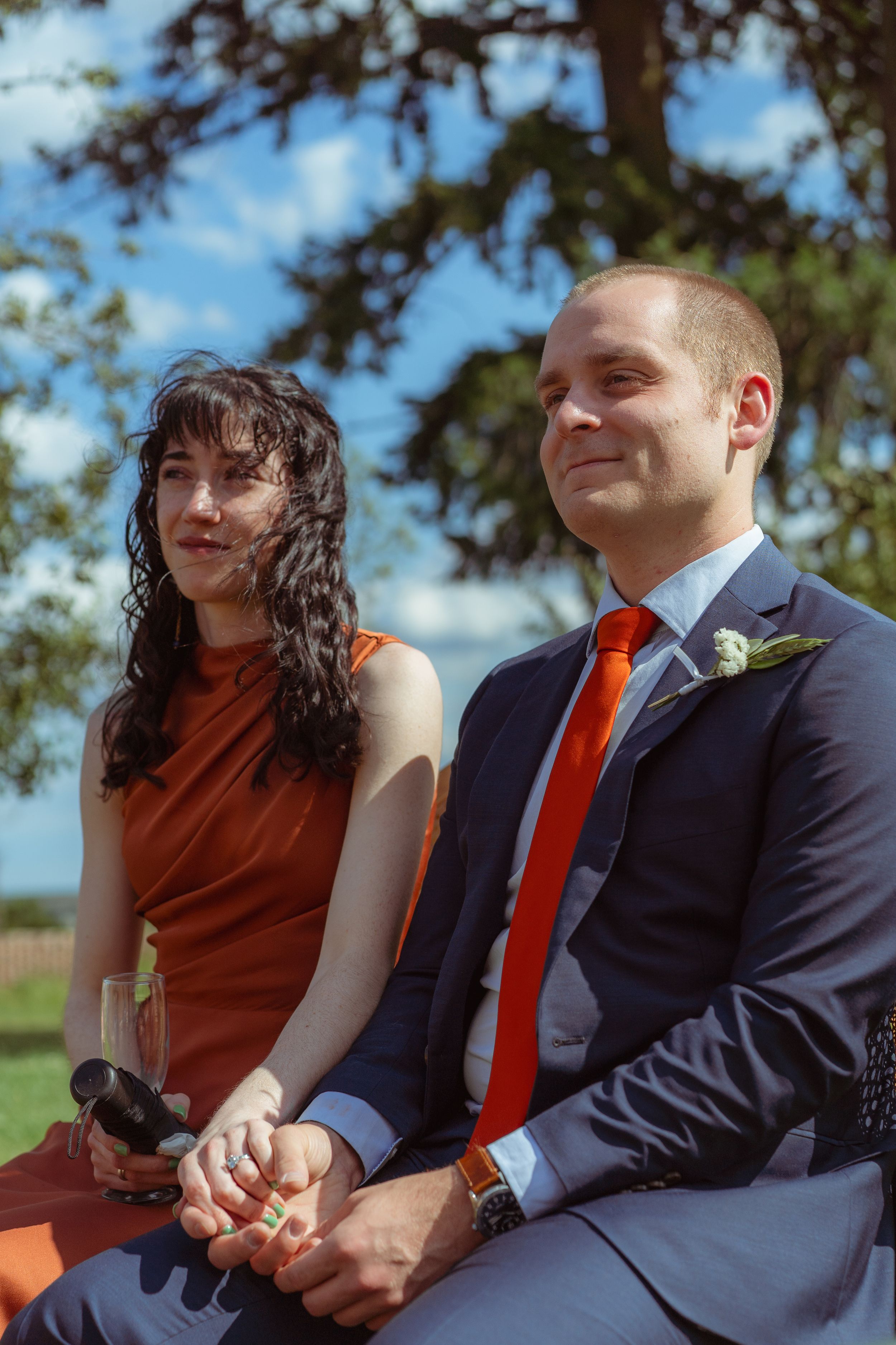 A couple watch the ceremony, sat outside on a sunny day