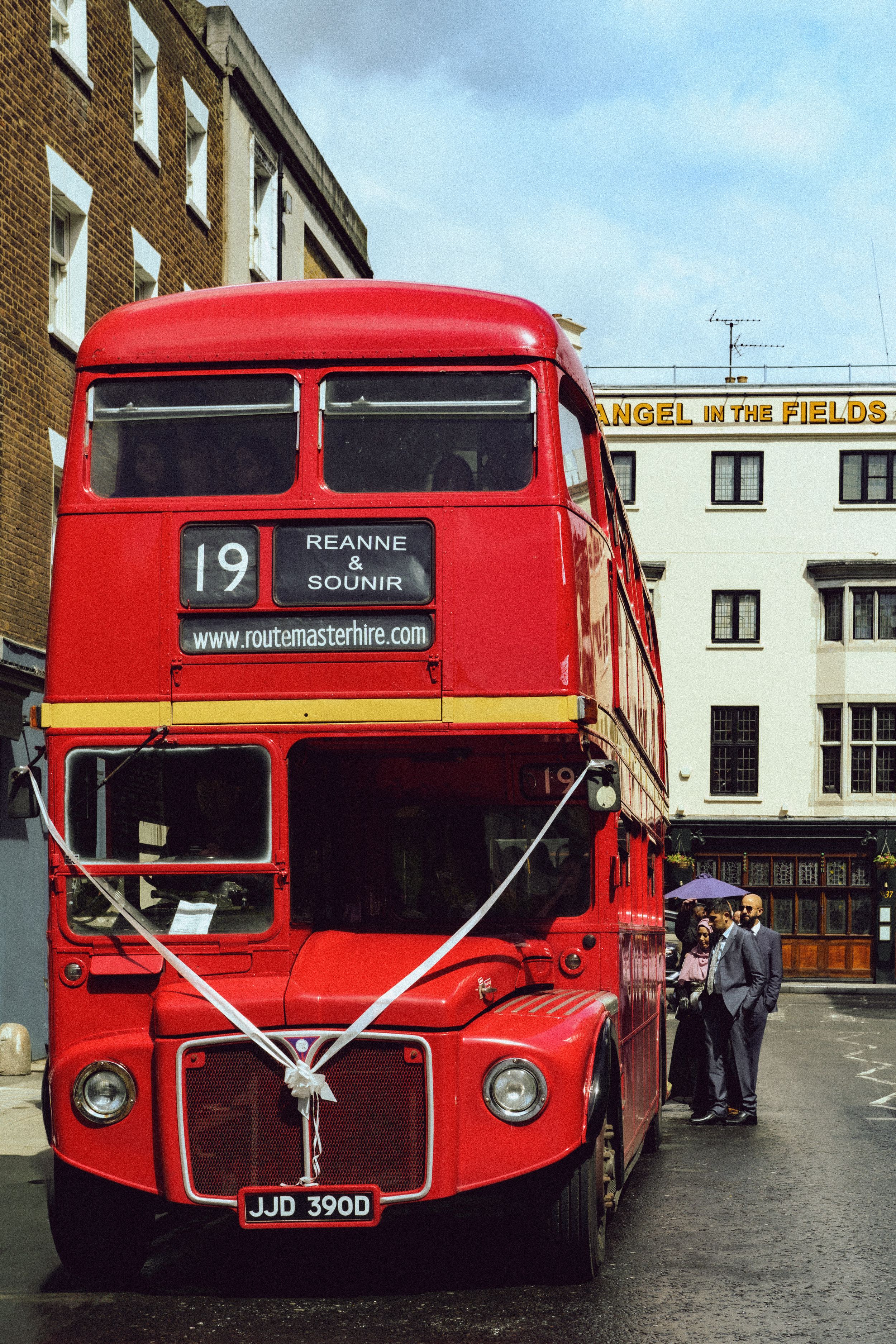 A red London bus with a wedding ribbon across the front