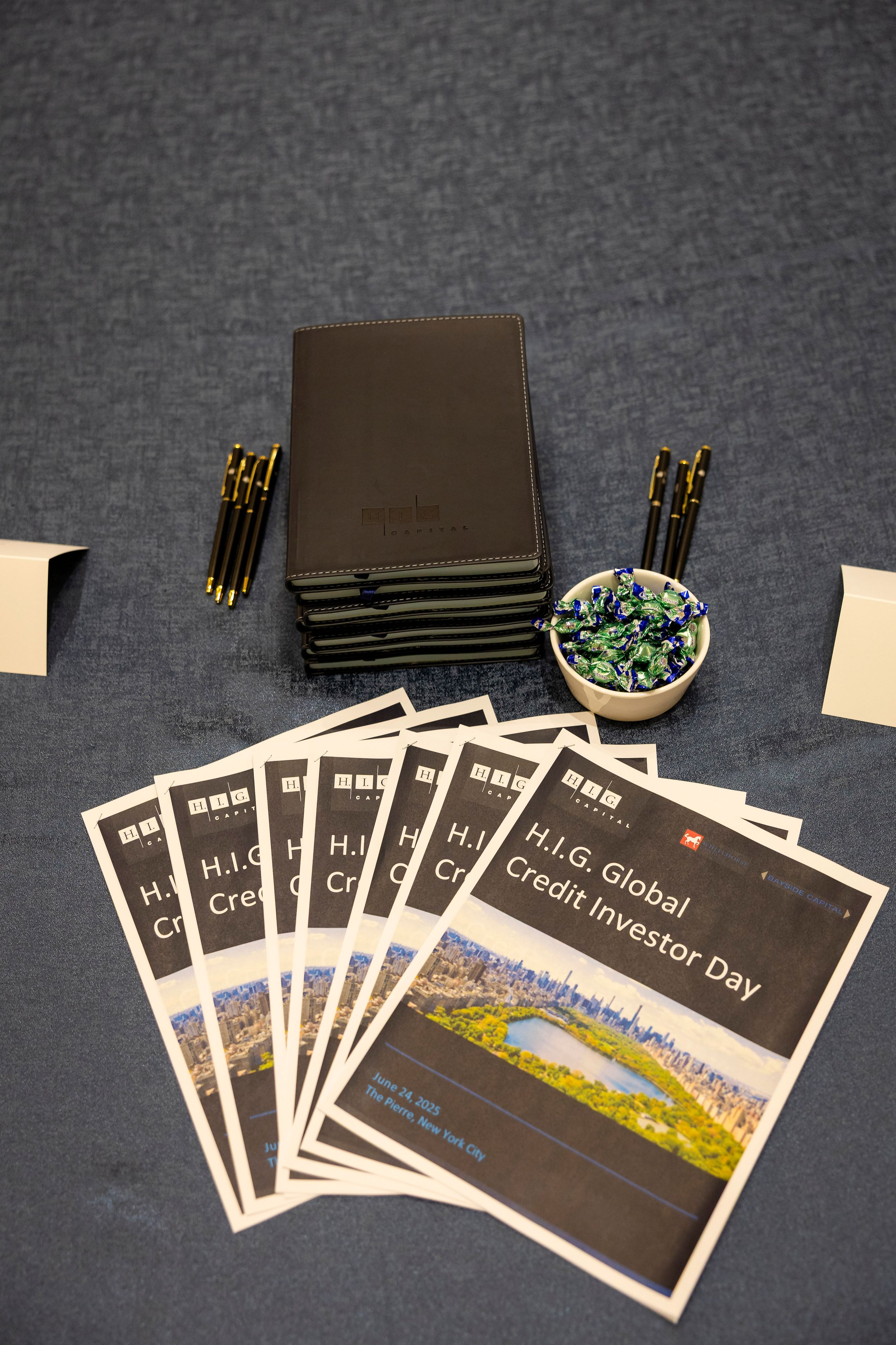 Black conference folders and materials arranged on gray surface for H.I.G. Global Credit Investor Day.