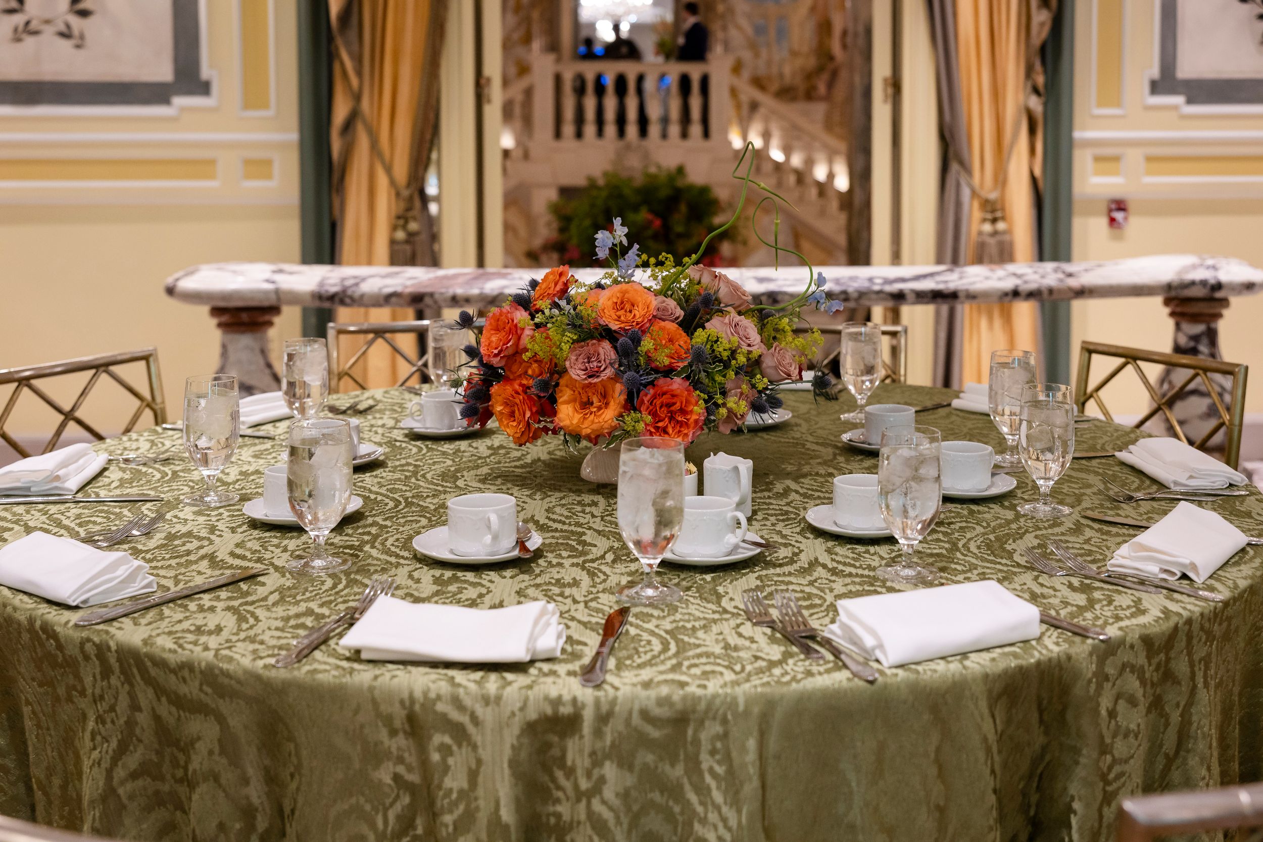 Elegant round dining tables with orange floral centerpieces and formal place settings.