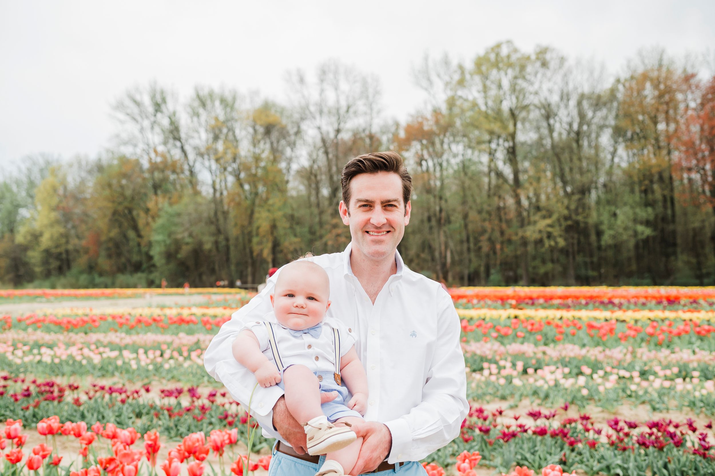 Family photo in a vibrant tulip field with blooming red and white flowers against a backdrop of spring trees.