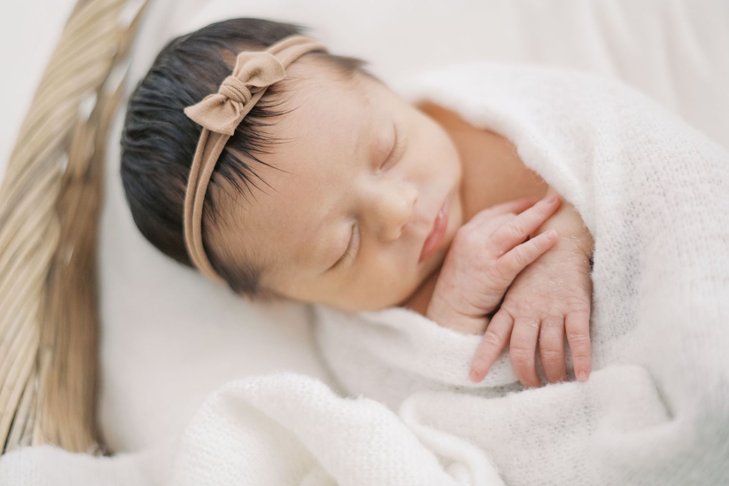 Peaceful newborn baby girl sleeping wrapped in white with a bow headband.