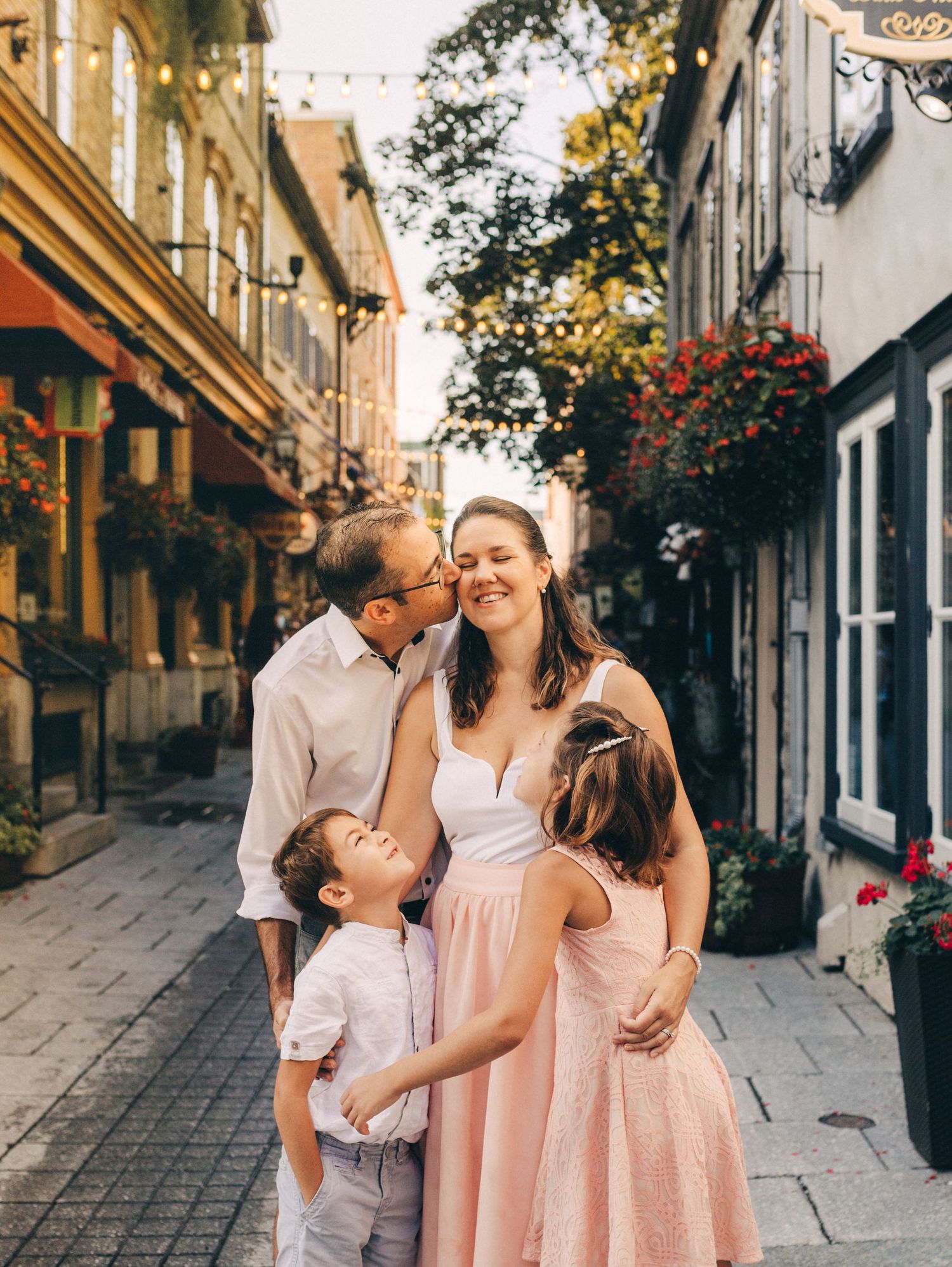 Intimate family moment captured on a charming cobblestone street lined with hanging flower baskets and historic buildings.
